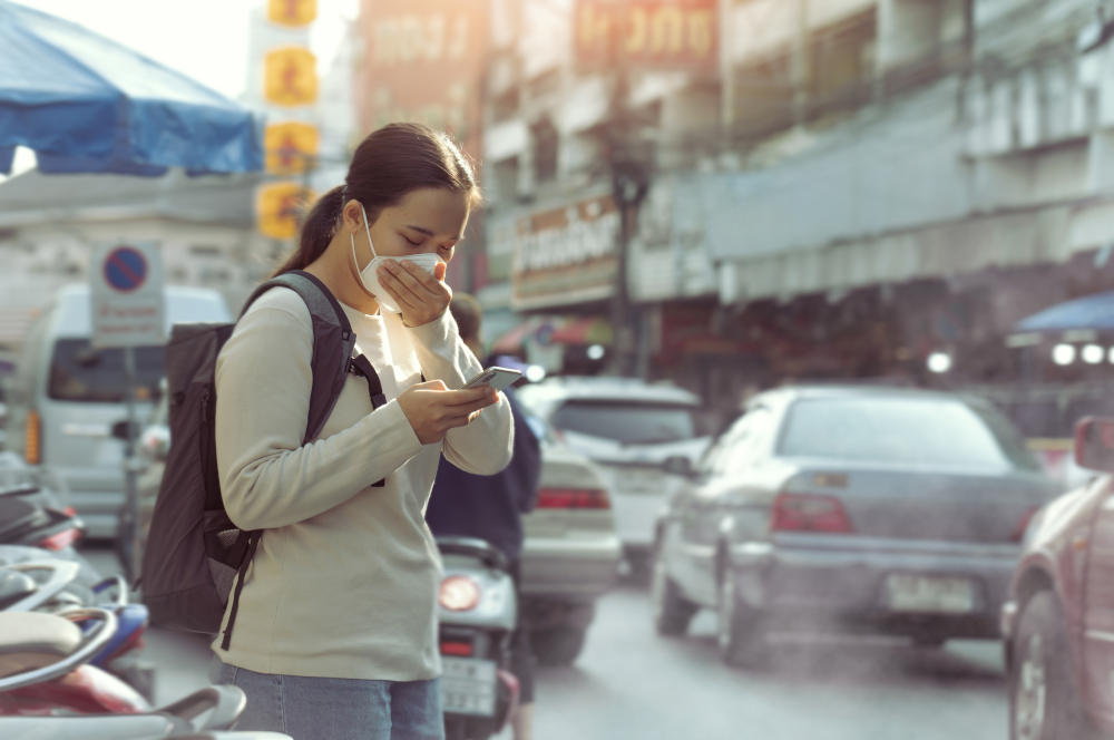 80 / 5.000 Shows a woman wearing a face mask in heavy city traffic looking at her mobile phone